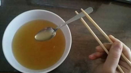 Someone using chopsticks to hold a spoon so they can eat their soup